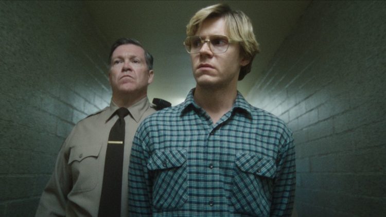 Evan Peters as Jeffrey Dahmer in a blue shirt in front of a cop in DAHMER Episode 5