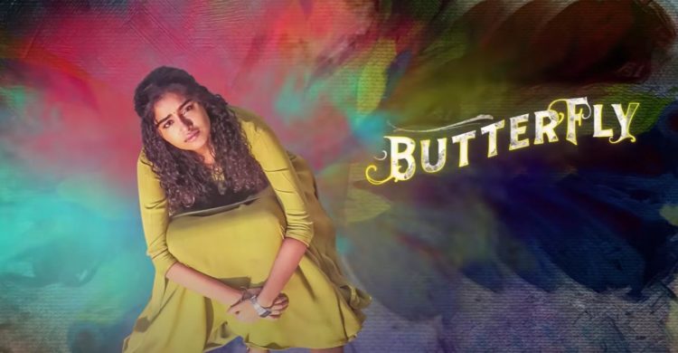Anupama Parameswaran looks upwards whilst sitting in a yellow dress for the title logo