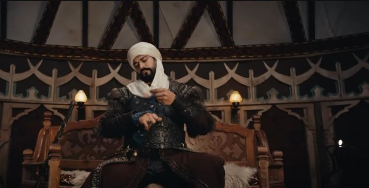 Osman Bey wraps his ring hand whilst sitting on his camp throne