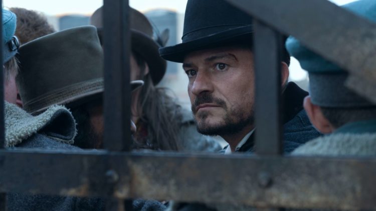 Orlando Bloom as Rycroft Philostrate in a bowler's hat looking through a gate in Carnival Row