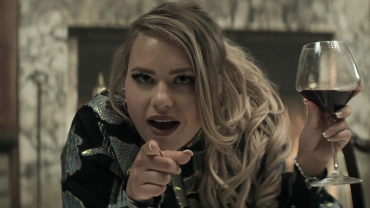 Eve Austin as Gemma holding a glass of wine and pointing in You season 4 episode 5