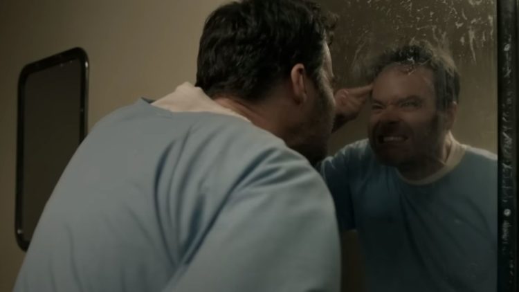 Bill Hader as Barry wearing blue prison overalls and pointing at himself in the mirror in Barry season 4
