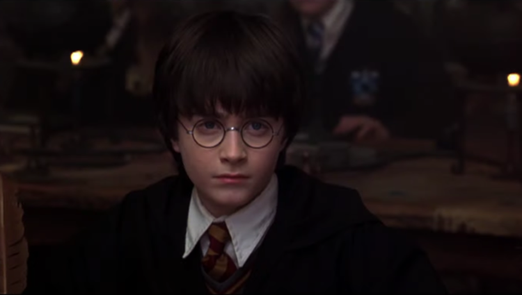 Daniel Radcliffe as Harry Potter wearing tie and robes sitting at table in Harry Potter And The Philosopher's Stone
